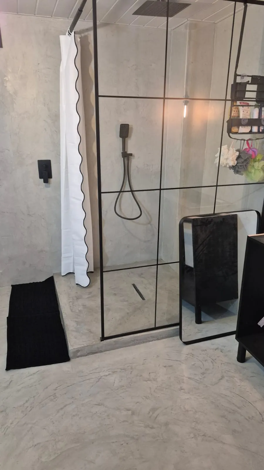 Walk-in shower with black-framed glass screen and microcement walls