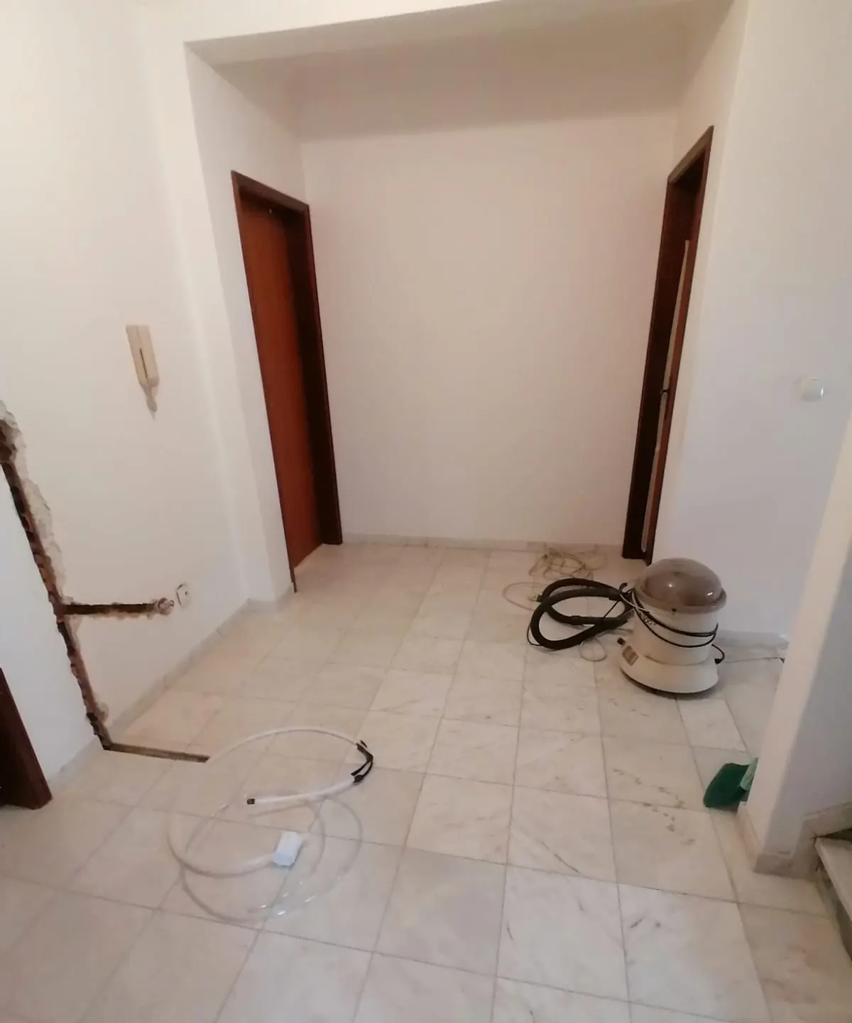 Before: hallway with old tiles, cables on the floor and an open wall chase