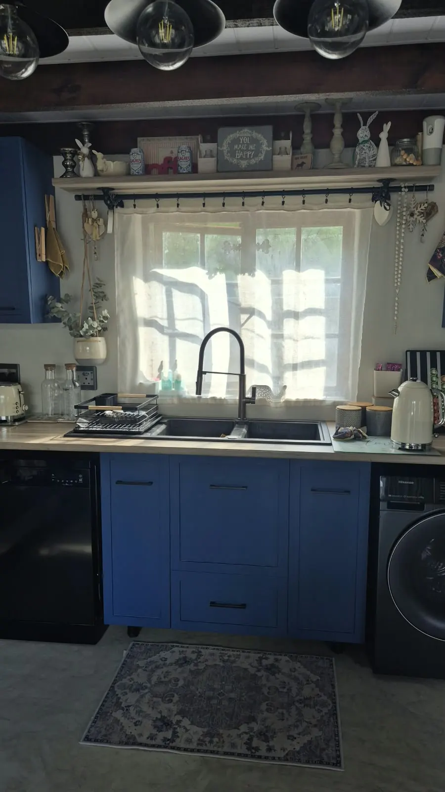 Black composite double sink under window with navy cabinets